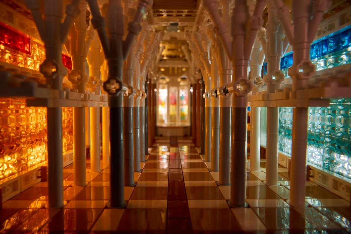 L'intérieur de la nef du LEGO Sagrada Família, colonnes claires et vitraux orangés à gauche, bleus et verts à droite
