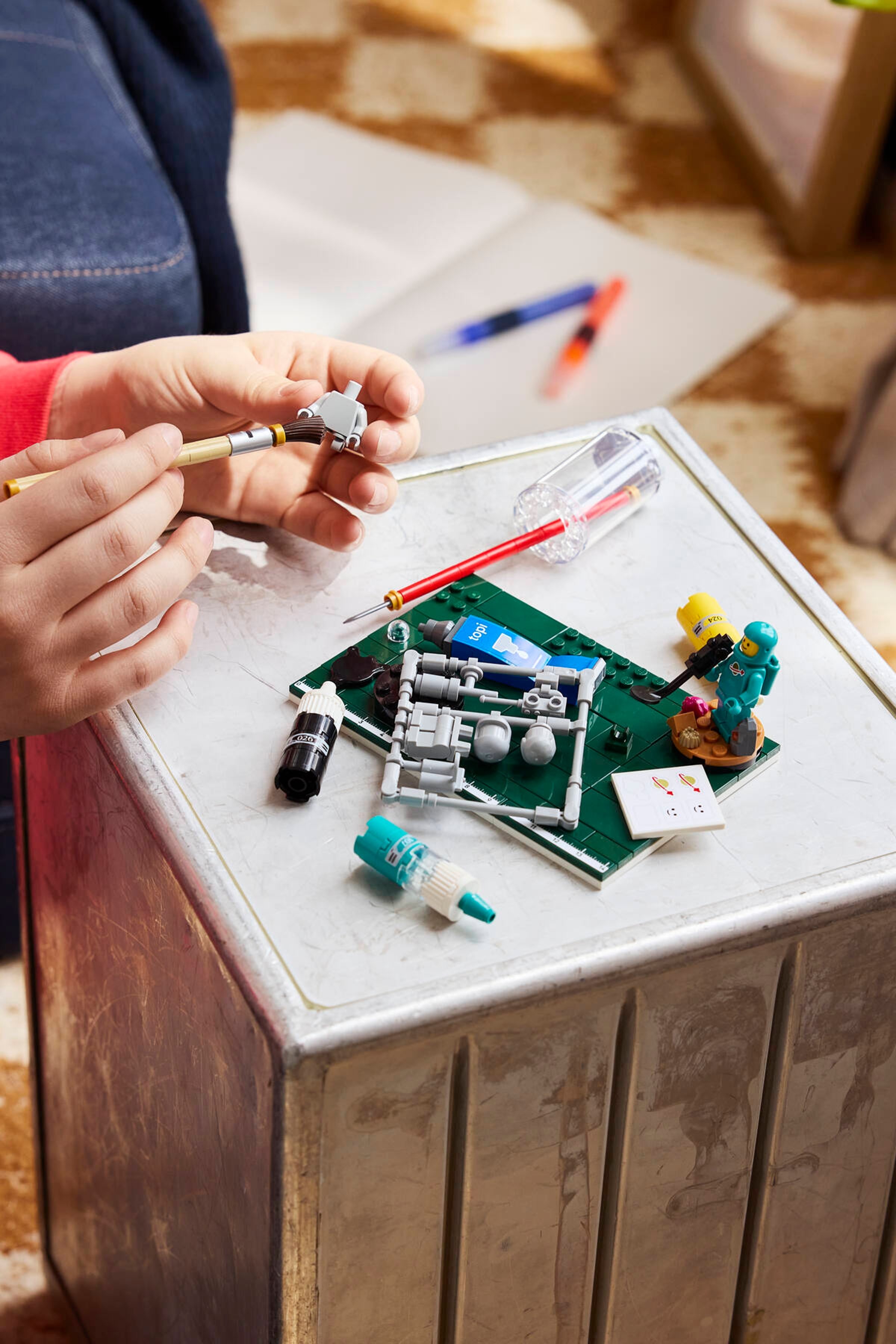 Une main peint une minifigurine grise à côté du set 40889
