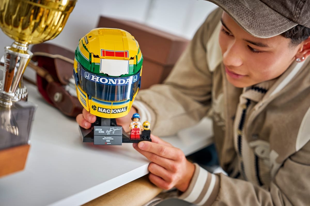 Le casque LEGO d'Ayrton Senna tenu à la main, avec sa plaque nominative et la minifigurine sur le socle
