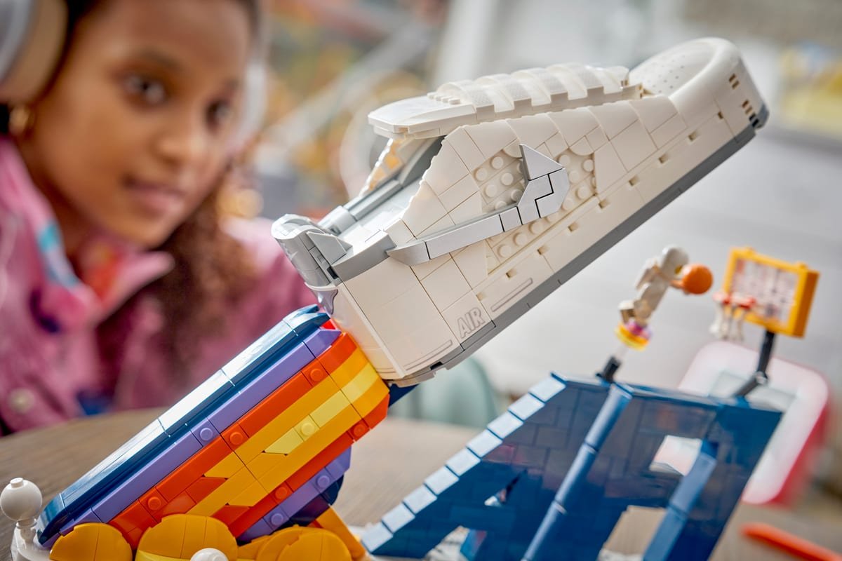 La sneaker LEGO inclinée sur sa rampe multicolore, avec la minifigurine d'astronaute et le panier de basket jaune