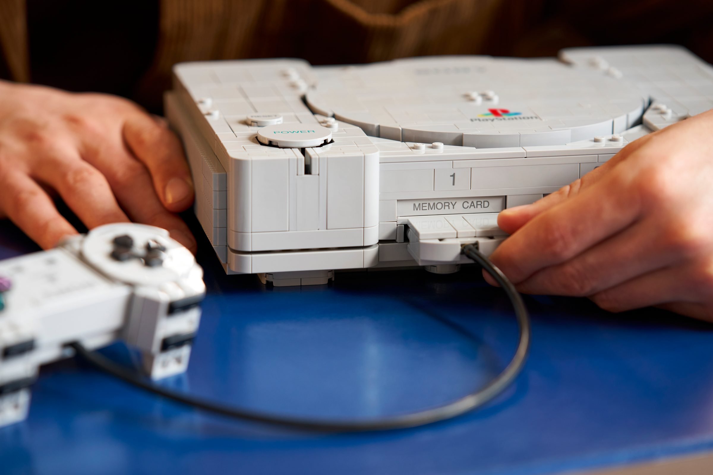 Deux mains branchent le connecteur de la manette dans la façade du LEGO PlayStation 72306