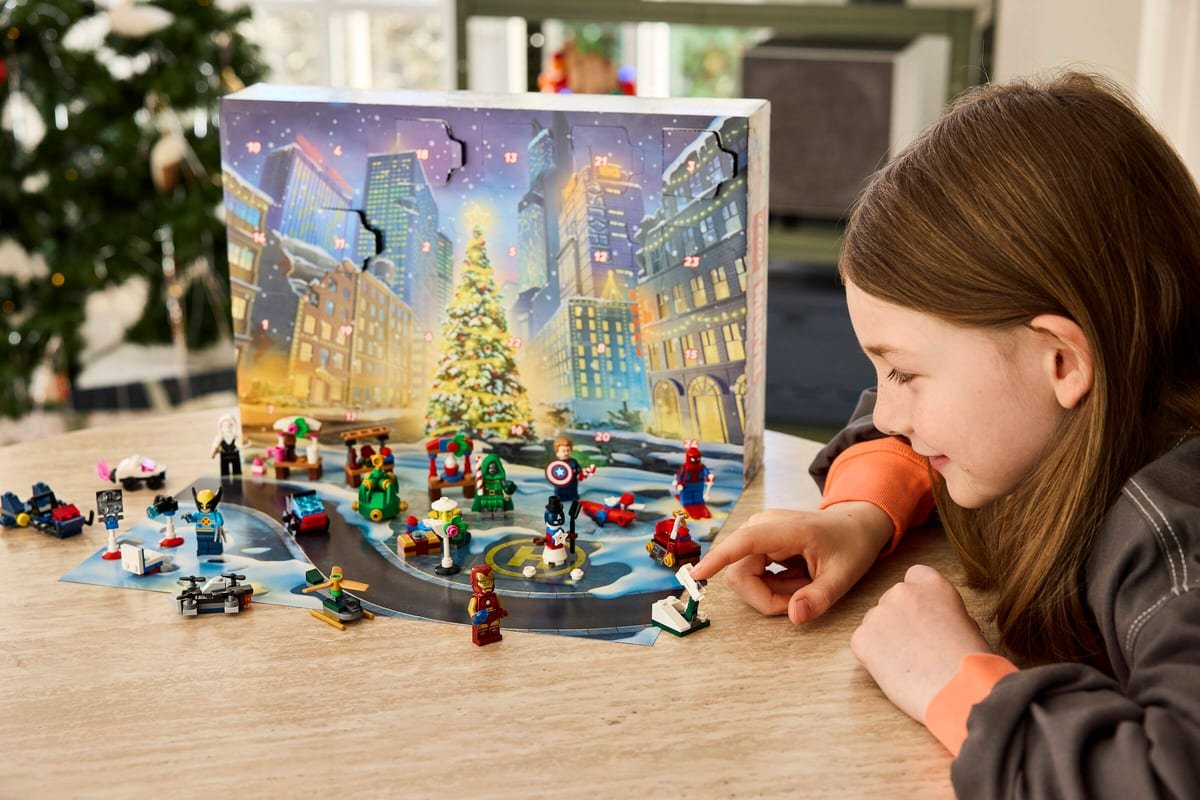 Une enfant assemble les modèles du calendrier LEGO Marvel devant un sapin de Noël